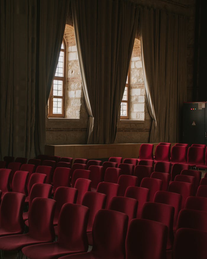 Cozy theater setting featuring luxurious red chairs and large window draped with curtains.