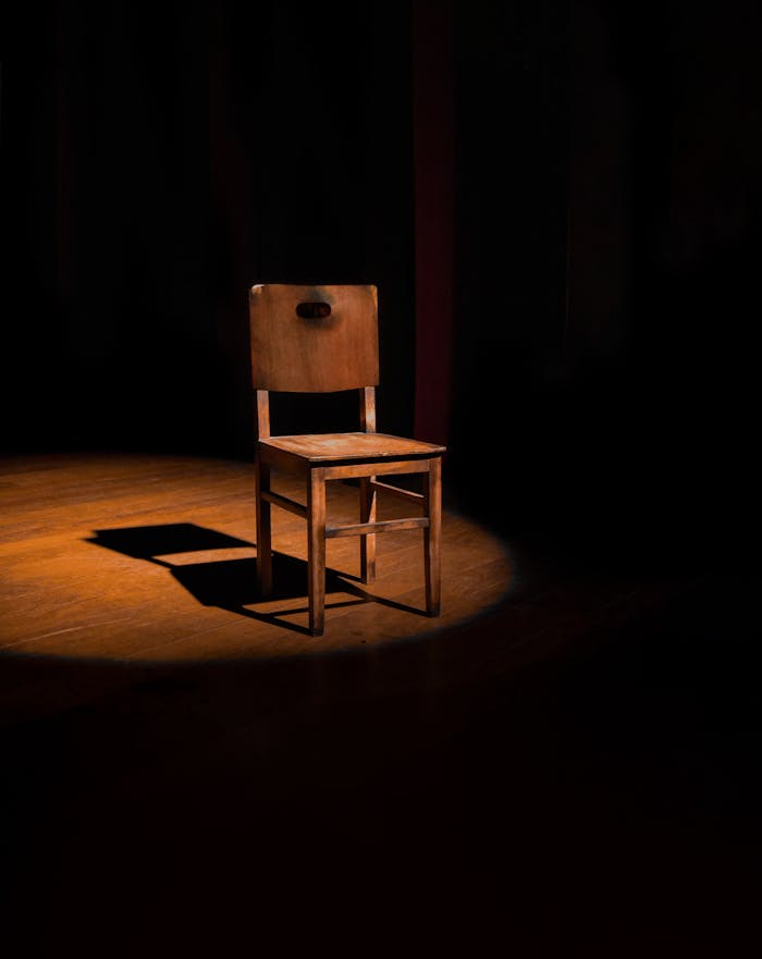 Elegant wooden chair illuminated by a spotlight creating dramatic shadows.