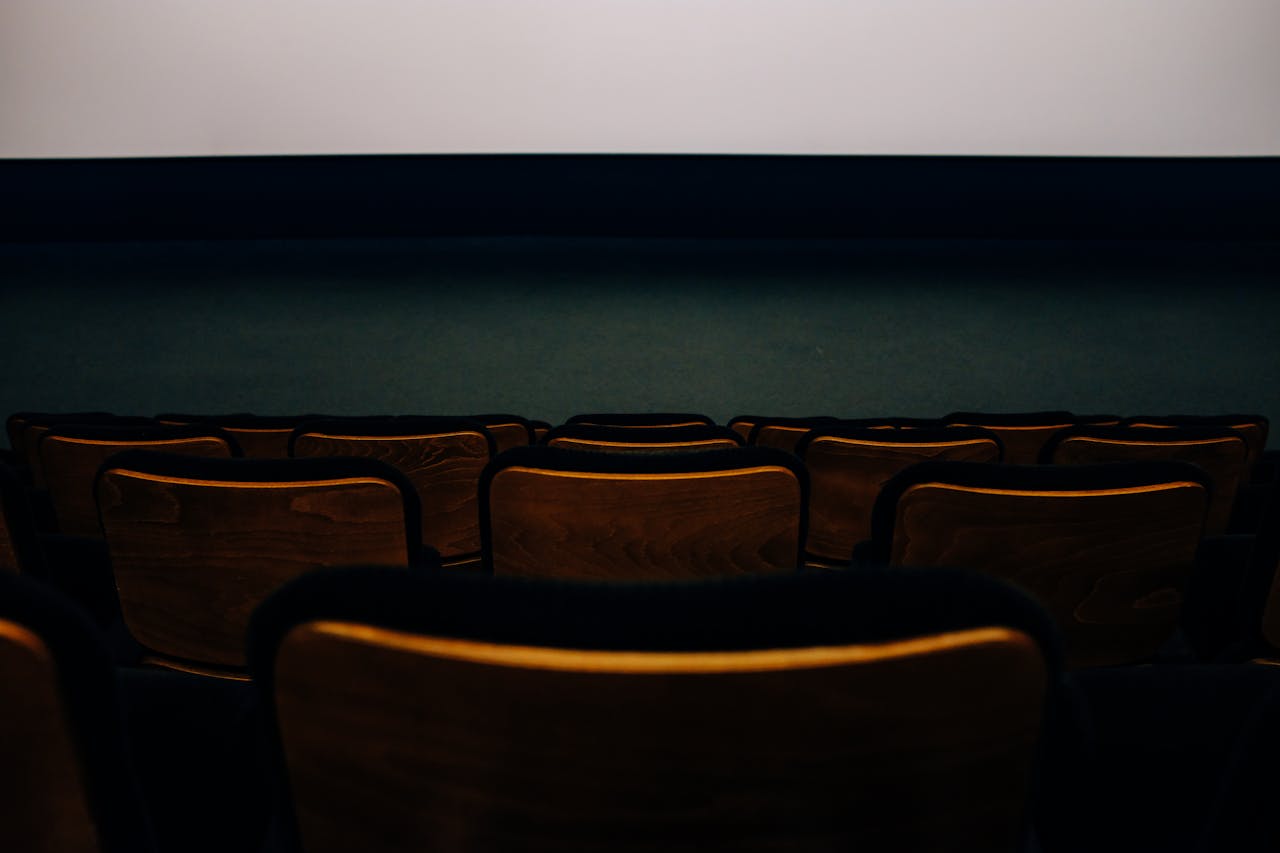 An empty auditorium with wooden seats facing a blank theater screen.